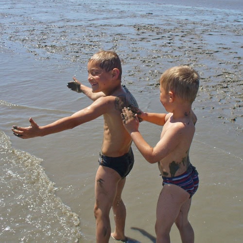 Zwei kleine Jungen im Wattenmeer: sie reiben sich genussvoll mit nassem Sand ein