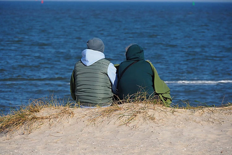 Paar sitzt unter eine Decke gehüllt am Strand von Schillig und schaut aufs Meer