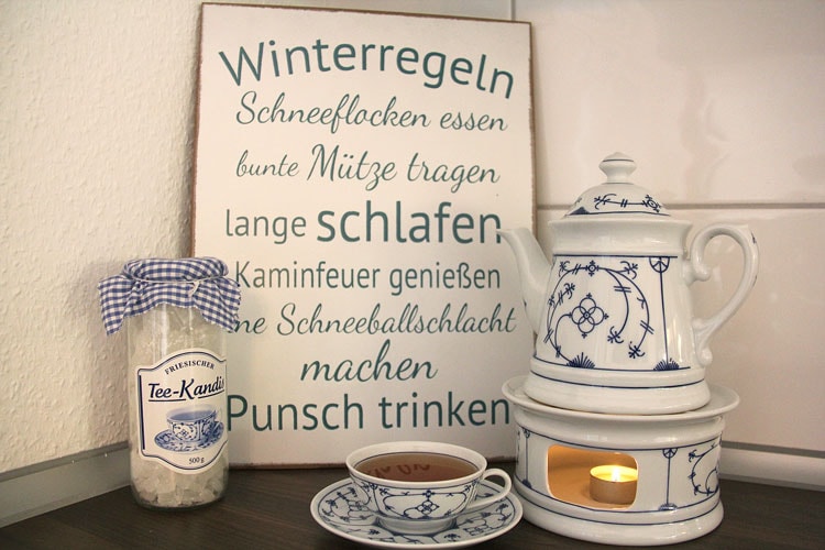 Friesenteekanne auf Stöfchen vor dem Schild "Winterregeln" mit dem Text: Schneeflocken essen, bunte Mützen tragen, lange schlafen, Kaminfeuer genießen, eine Schneeballschlacht machen, Punsch trinken
