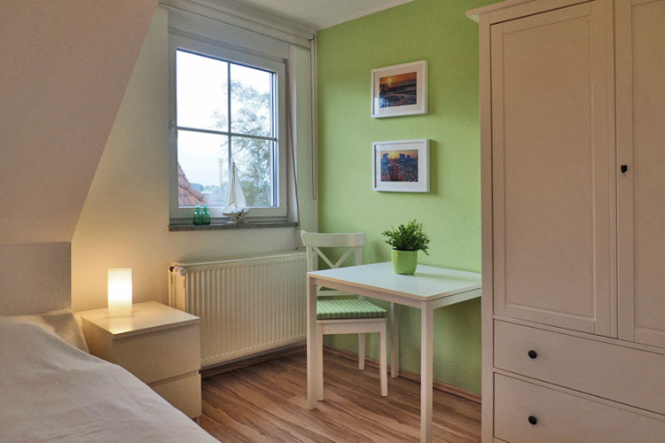 Helles geschmackvoll eingerichtetes Kinderzimmer: mit weißem Nachttisch, Stuhl mit hellgrünem Kissen, mit Tisch und Schrank, vor einer hellgrünen Wand