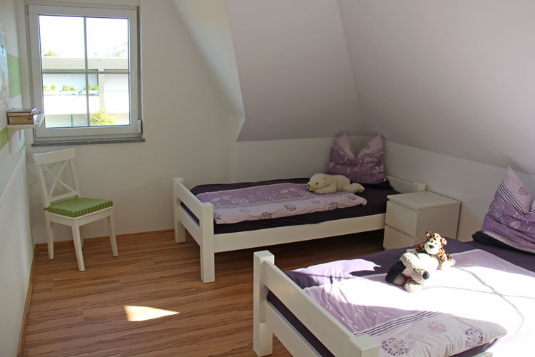 Im lichtdurchfluteten Kinderzimmer stehen zwei Betten jeweils mit einem Nachttisch. Auf jedem Bett wartet ein Stofftier auf die kleinen Gäste