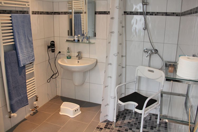 Barrierearmes Bad mit ebenerdiger Dusche und Duschstuhl und unterfahrbarem Waschbecken.