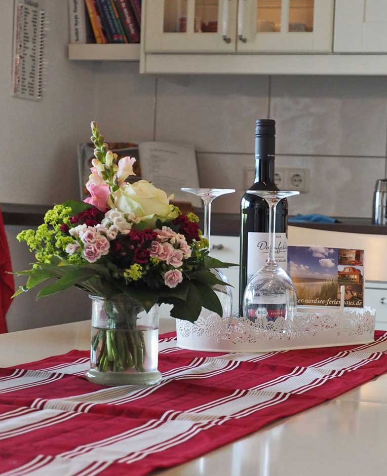 Ferienhaus-Esstisch mit Blumenstrauß und Weinflasche zur Begrüßung