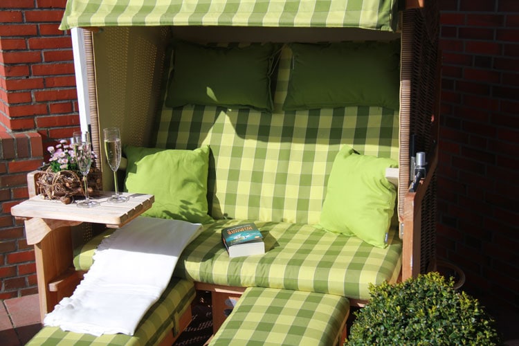 Der gepolsterte Strandkorb mit einem Buch und zwei Gläsern Sekt