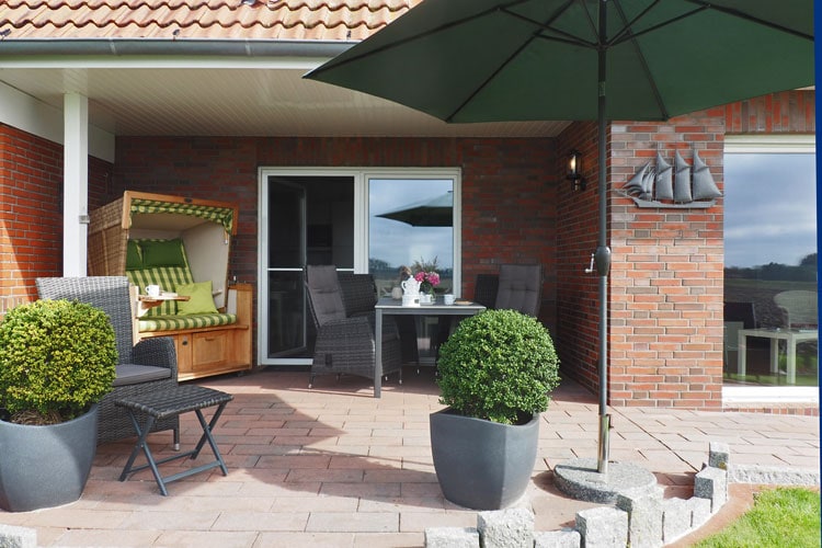 Gepflasterte Terrasse des Ferienhauses mit Sonnenschirm, Strandkorb und Sitzecke