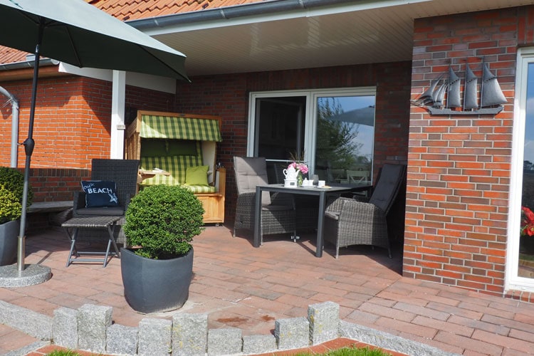 Gepflasterte ebenerdige stufenlos zugängliche Terrasse mit Sitzecke, Strandkorb und Sonnenschirm.