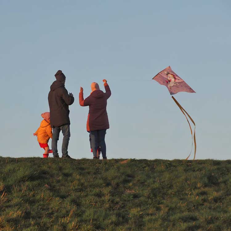 Familie mit kleinen Kindern lässt auf dem Deich Drachen steigen