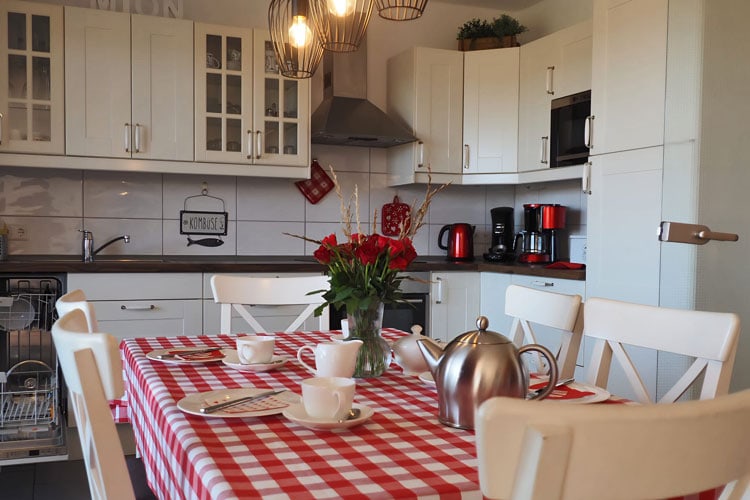 Blick auf gedeckten und mit Blumen dekorierten Esstisch, dahinter die Küche im modernen landhausstil